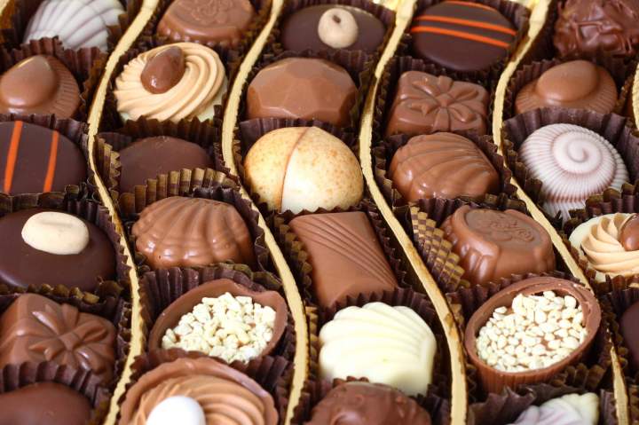 Une boîte ouverte de chocolats artisanaux variés, avec des formes et des décorations différentes, prêts à être dégustés.
